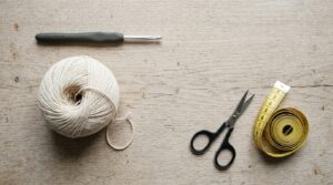 a five millimetre crochet hook a ball of cream cotton yarn scissors and a tape measure laid on pale wood